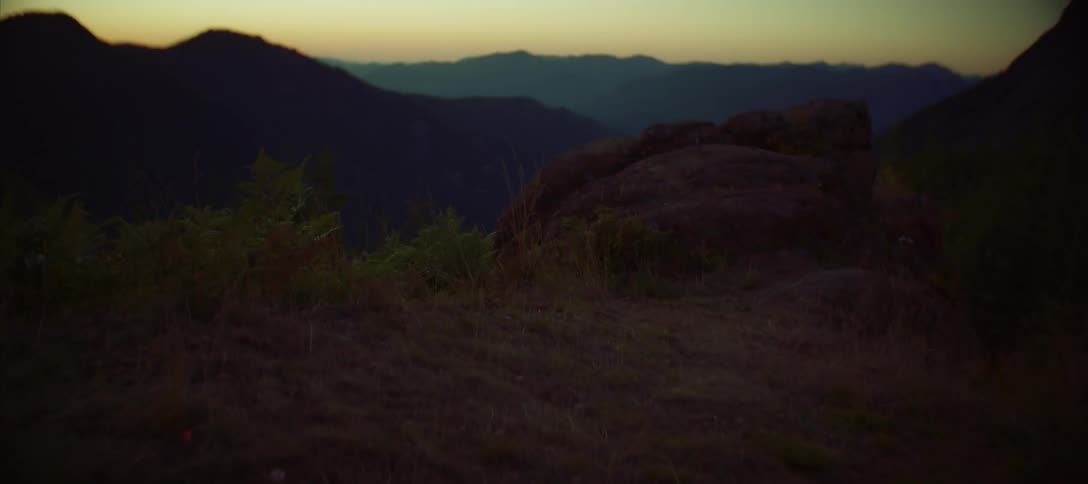The camera pans up from the ground to reveal a series of mountains at sunset