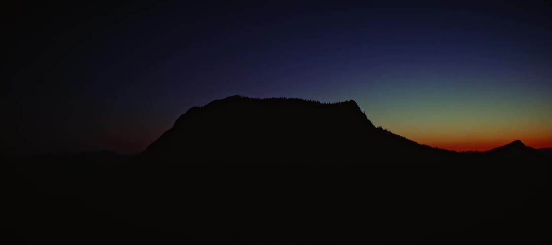 A dark mountain silhouette is set against a colorful twilight sky