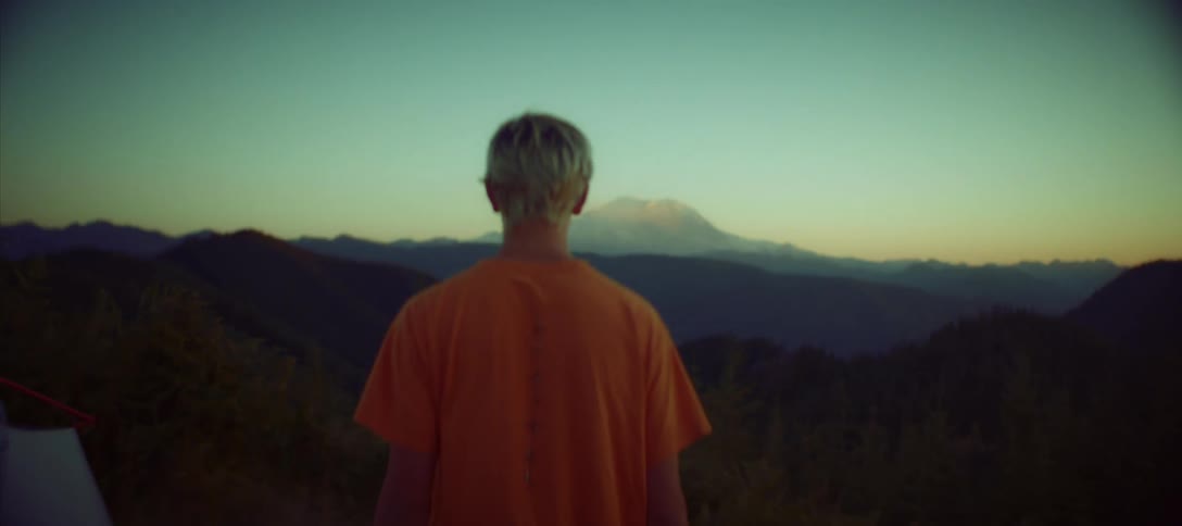 A person is walking away from the camera at a campsite toward a view of a mountain range