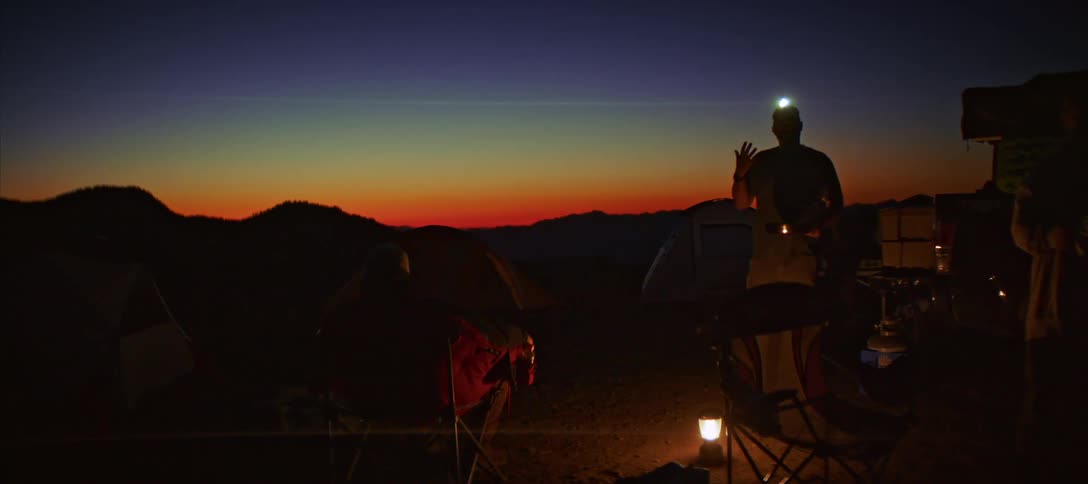 Silhouette of travelers at a campsite at night with the silhouette of mountains on the horizon