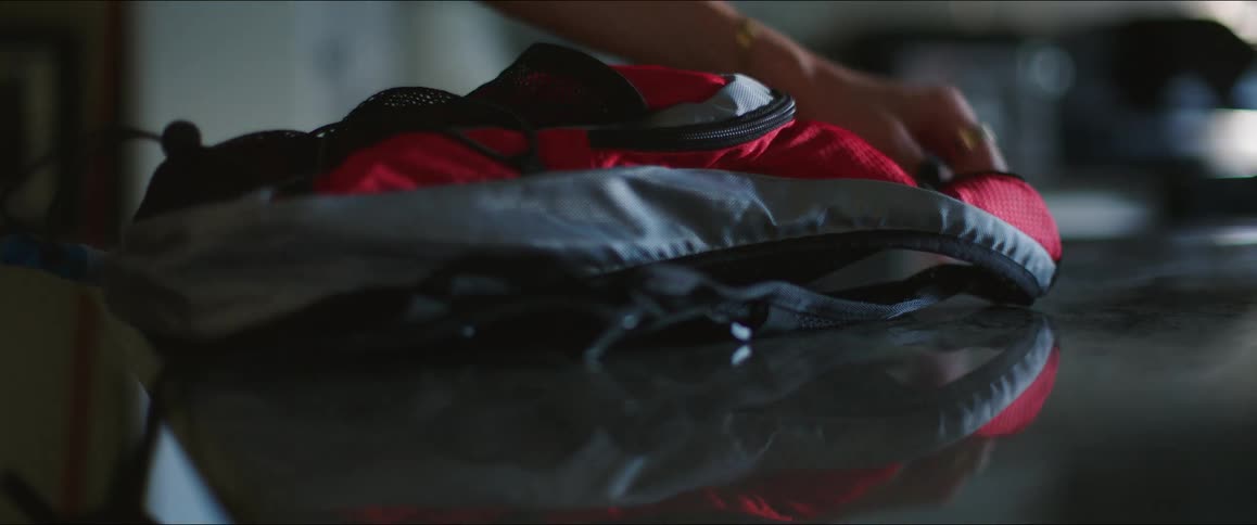 A hand picks up a smartphone and backpack from a table indoors