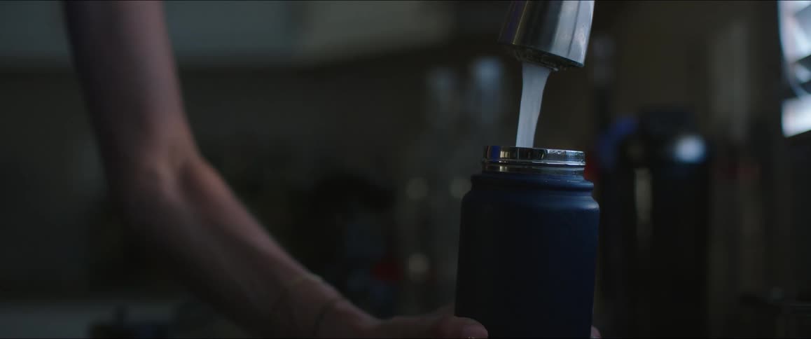 A tight shot of a kitchen faucet shows a person filling up a blue reusable water bottle the clear stream of water is visible as it flows from the faucet into the bottle