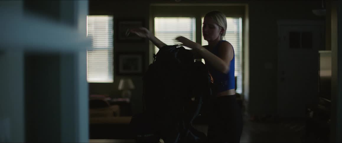 Woman finishes packing a backpack before picking it up and heading towards the outside door during the daytime