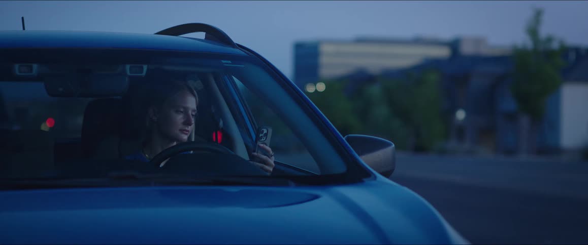 A woman gets into a car closes the door and looks down at a phone