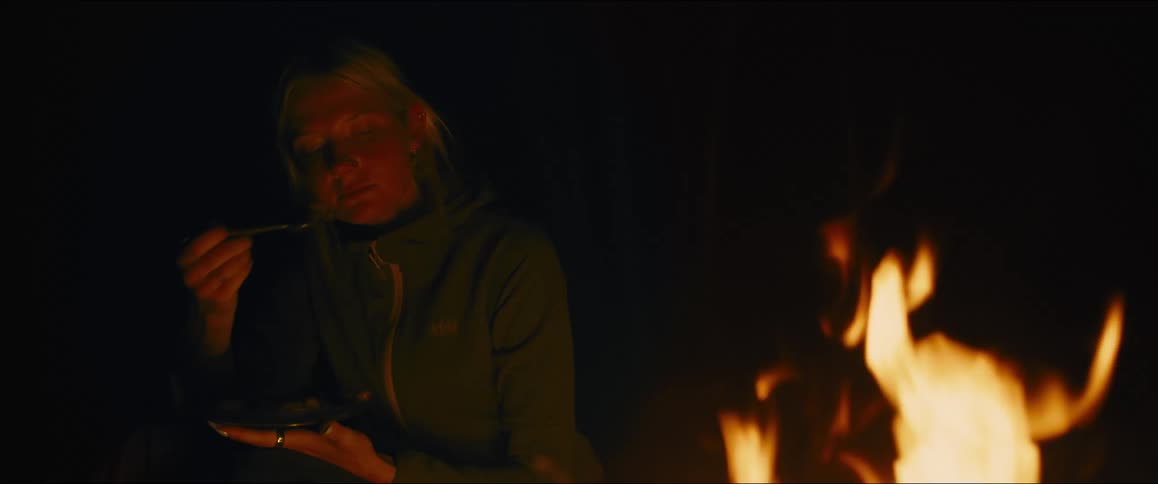 The woman is eating by the campfire