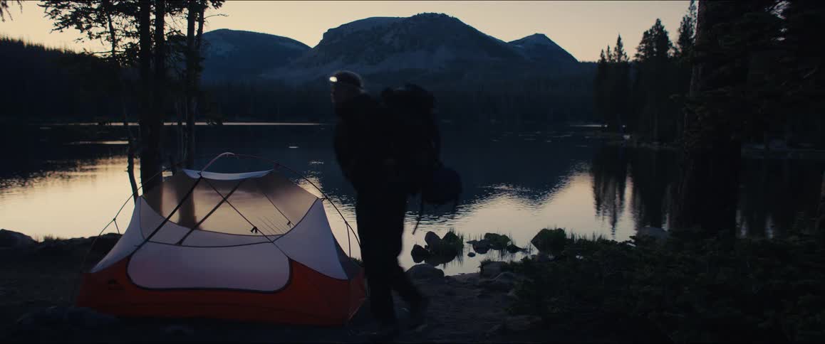 Person walks by a mountain lake with a backpack at dusk