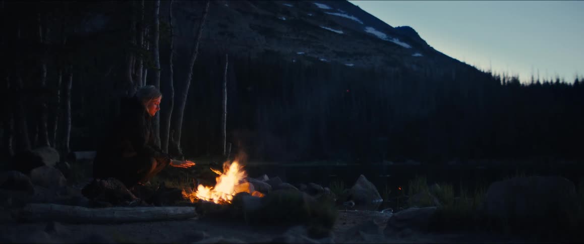 Woman warming herself by a campfire on a mountain at dusk