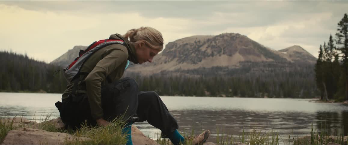Woman sitting by a lake tying her hiking boots