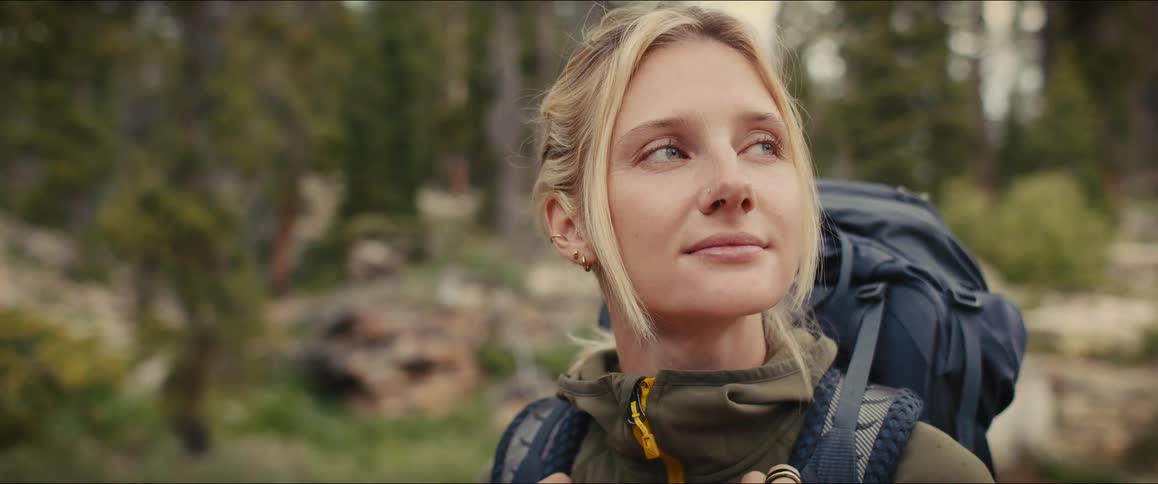 A woman smiles while gazing ahead on a hike with a backpack