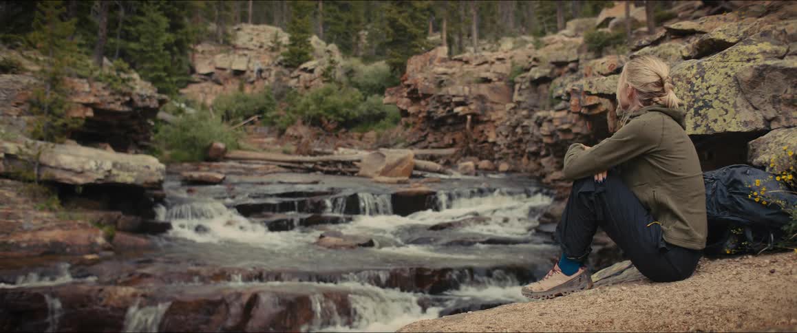The woman sits by the creek