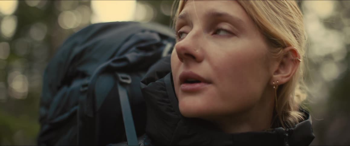 Woman hikes with a backpack gazing ahead through the forest