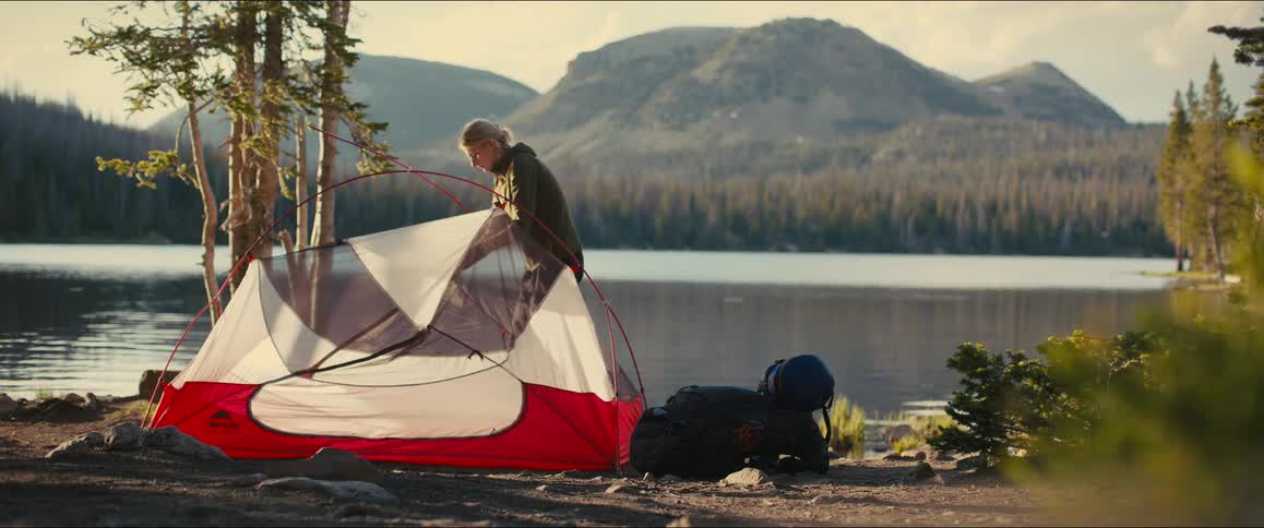 The woman is setting up a tent by the lake