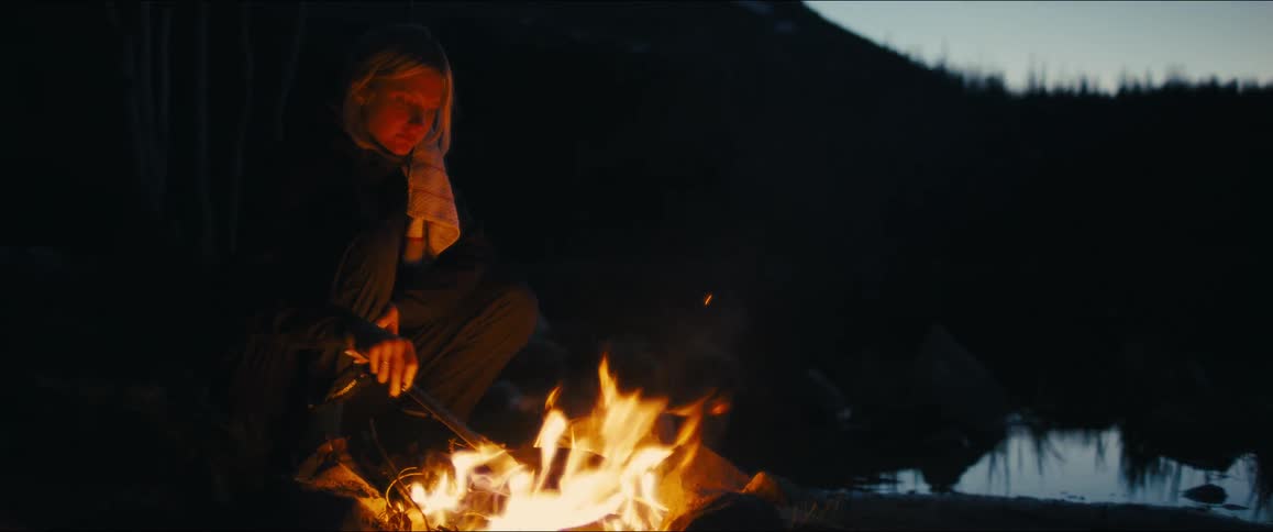 A woman cooks over a campfire in the wilderness at night