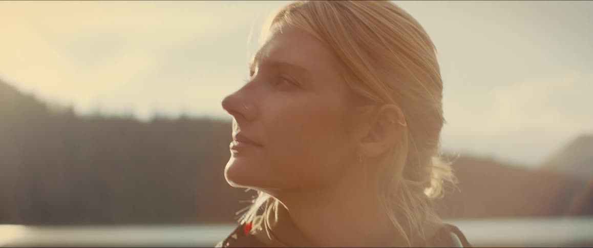 In a closeup a woman on a boat looks around at the scenery with a serene expression her face lit by warm sun rays as a light rain begins to fall