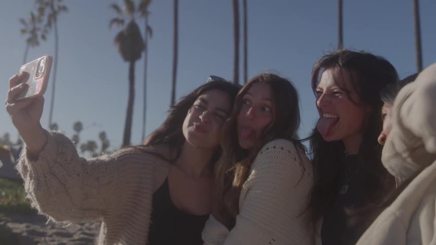 Female friends make faces while posing for a group selfie as they stand outdoors on a sunny day