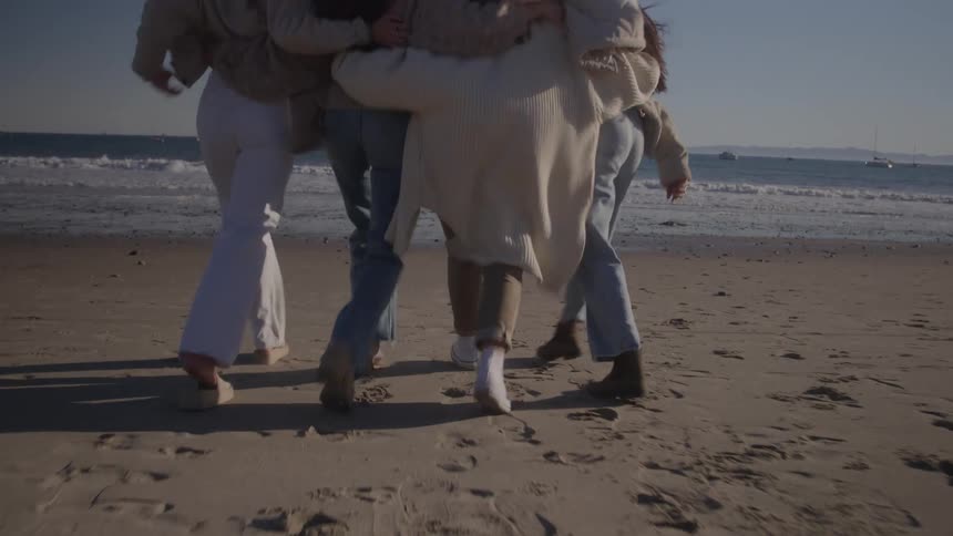 Four friends hugging each other walking on the sand towards the sea