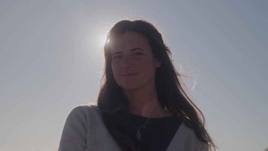 A smiling woman looks into the camera under a bright sun