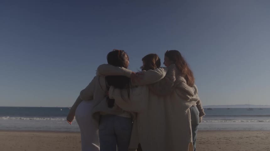 Four women and friends hugging each other on the beach sand