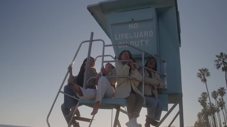 Four friends sitting at a lifeguard stand and laughing