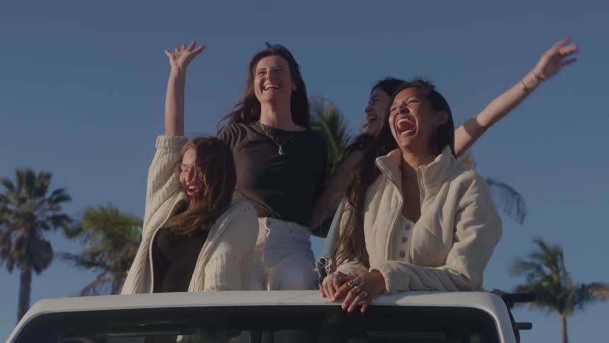Female friends stand in a car smiling and posing on a sunny autumn day