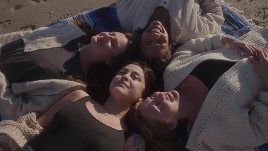 Four smiling friends lying on a towel in the sand