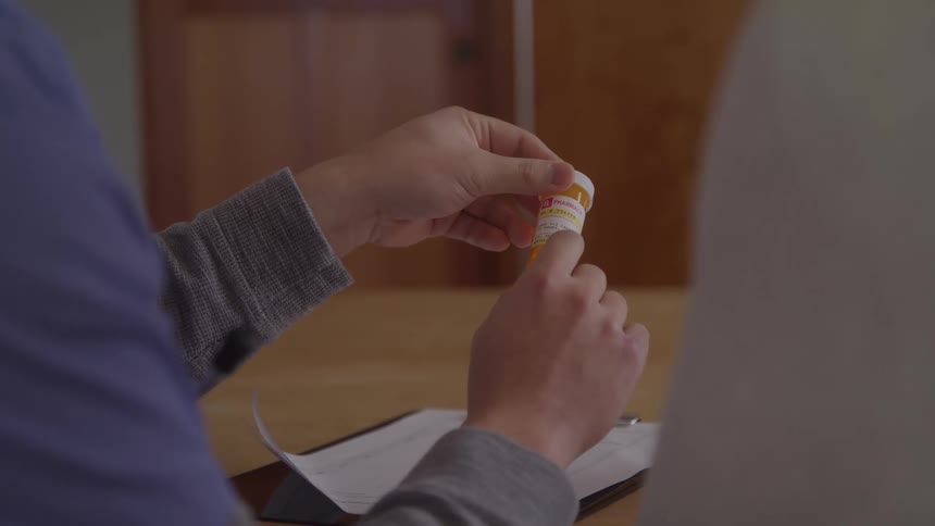 A pair of hands is shown in a closeup holding a prescription pill bottle they attempt to open the childproof cap twisting and pressing on it
