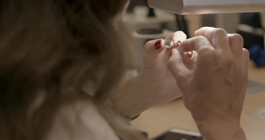 A woman rolls two jewels around in her fingers under a light