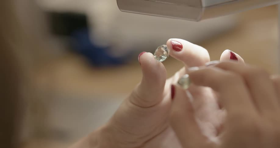 A person is examining two jewels under a light