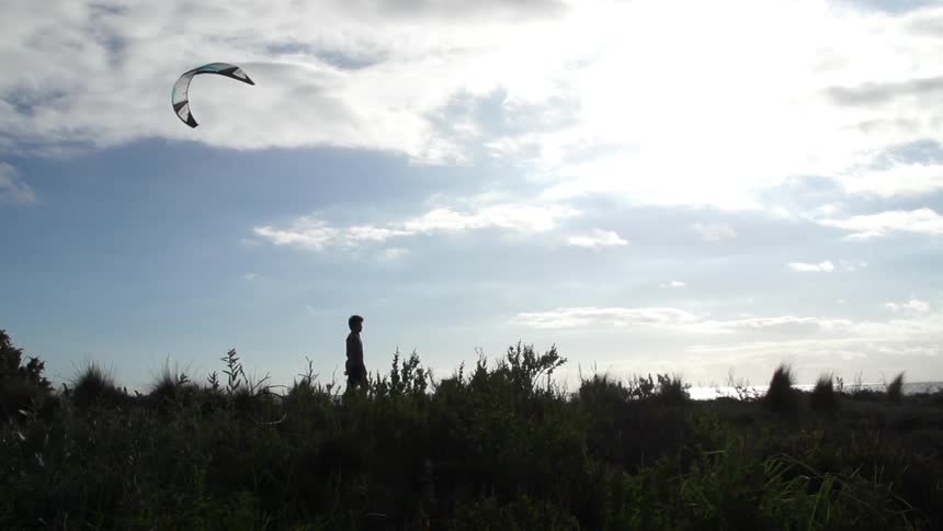A boy walks across a field as a kite flies above