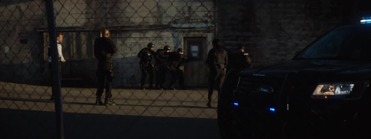 A video game scene of a group of armed officers in tactical gear who appear tense and focused while surrounding a building at night