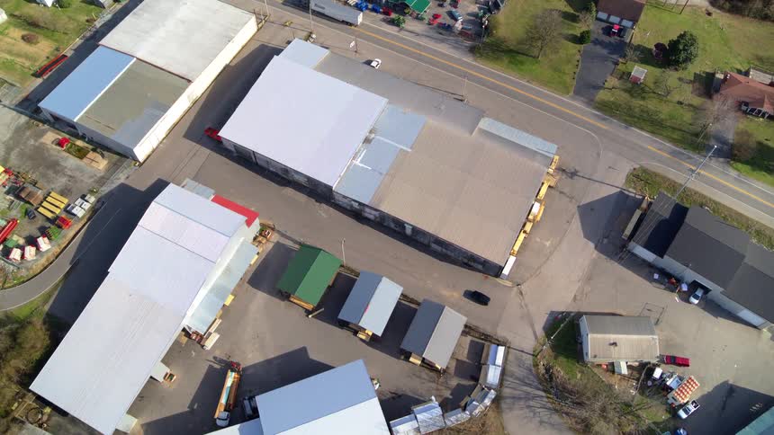 An aerial view shows a cluster of large warehouse buildings along a main road