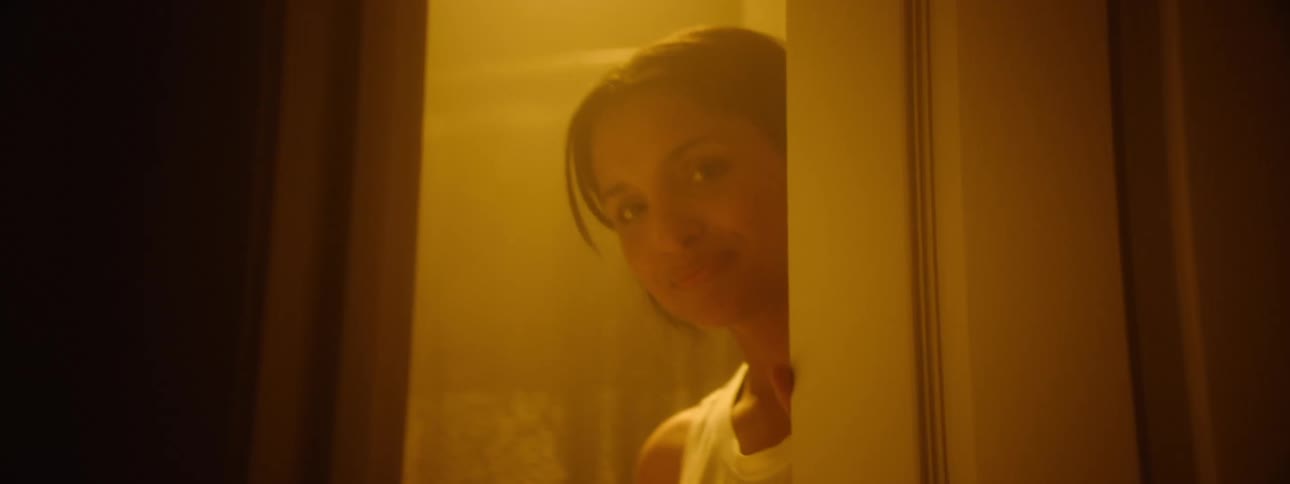 Young woman indoors smiling as she opens a bathroom door while holding a pair of scissors