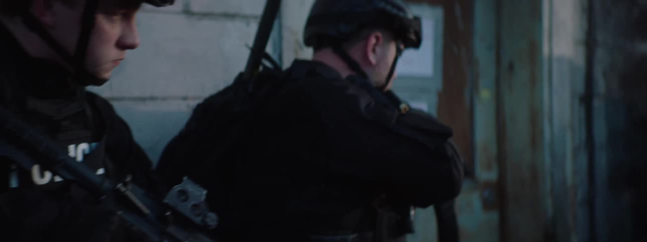 A group of men in tactical gear with weapons are standing by a concrete wall