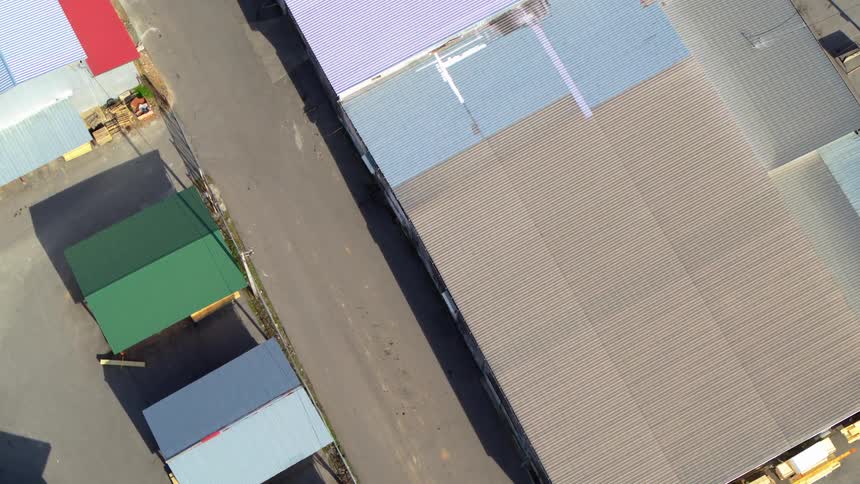 An aerial shot slowly descends over an industrial area featuring various warehouses and sheds with colorful corrugated metal roofs