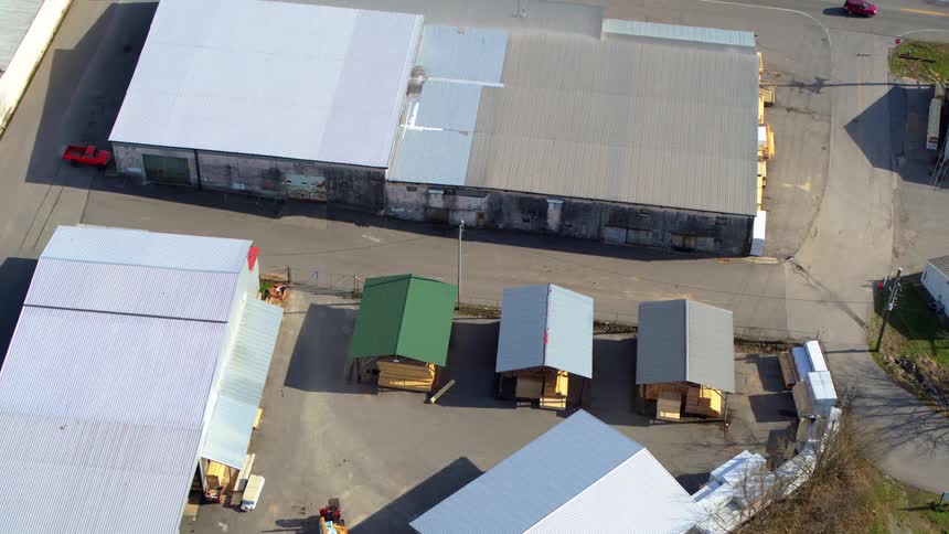 An aerial shot captures a large industrial area with several warehouses and a long wide street the camera slowly pans out revealing more of the surrounding area and a few small shedlike structures in a lot between the buildings