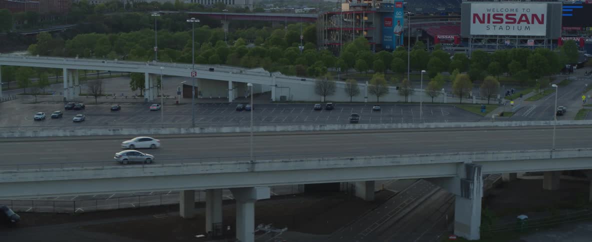 An aerial drone shot pans across a large busy highway with several lanes of traffic the camera then moves to capture a wide view of the city skyline showing many tall buildings and a large bridge over a river with cars crossing both