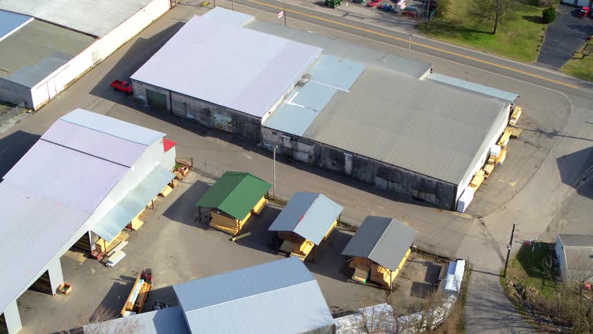 An aerial view captures several warehouses and storage sheds in a lumber yard beside a main road