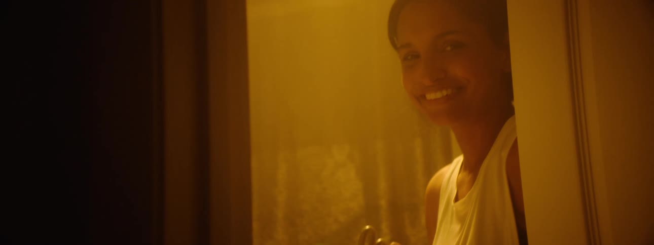 A person holds up a pregnancy test box labeled right time which they open to reveal the test inside the camera then pans up to show a young womans face peeking from behind a door with a hopeful happy smile suggesting the test has confirmed a positi