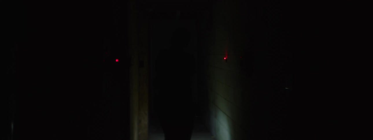 A female police officer walking in a dark hallway full of explosives in the walls holding a flashlight
