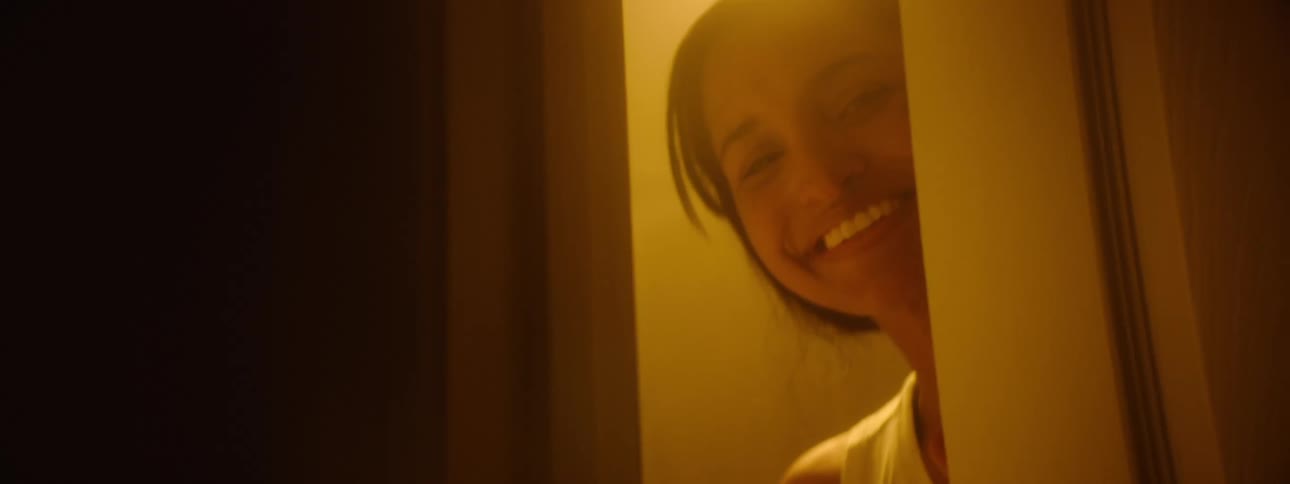 A young woman is closing slowly a door with a smile on her face