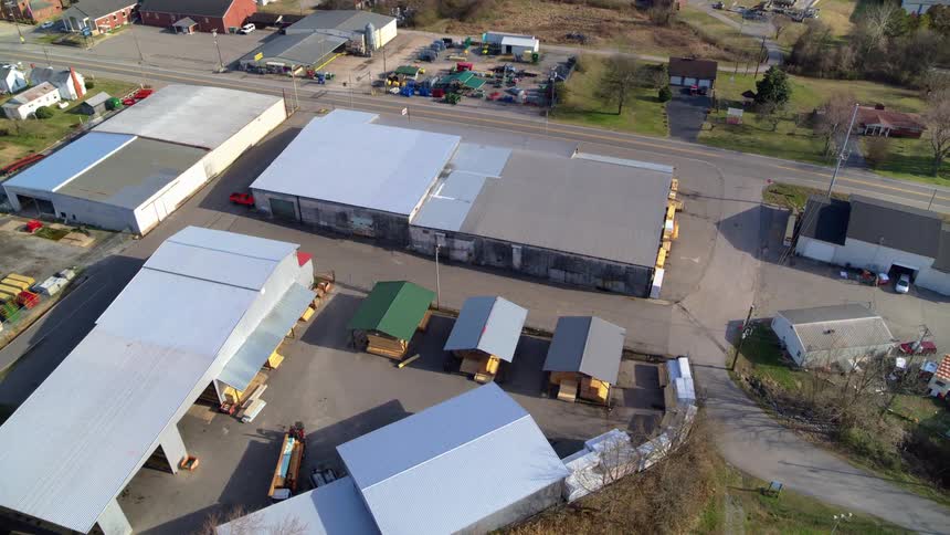 An aerial drone shot pans over a large commercial area featuring several industrial buildings and parking lots the camera then moves to show a clear view of a rural town with many houses and small businesses surrounded by green lawns and bare trees