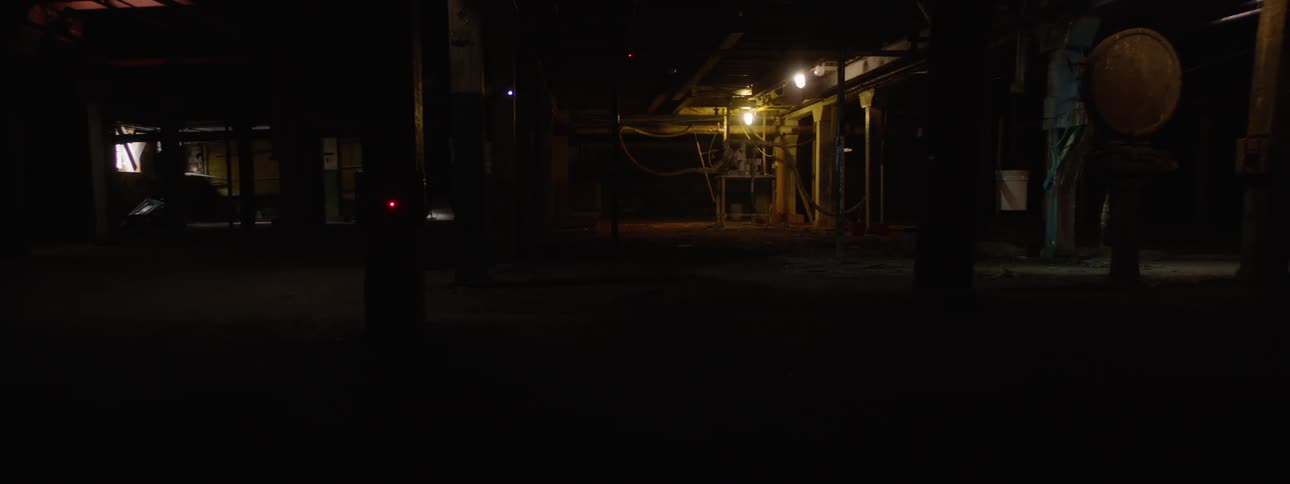 A person walking across a building at night with faint lightning in the background