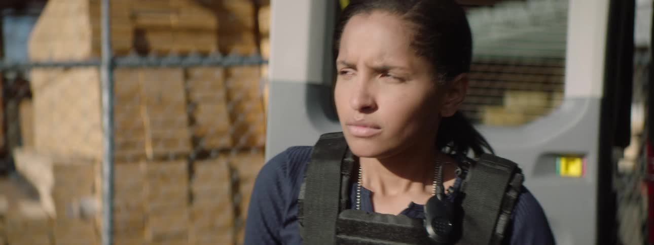 Woman wearing a tactical vest in an area surrounded by stacked lumber