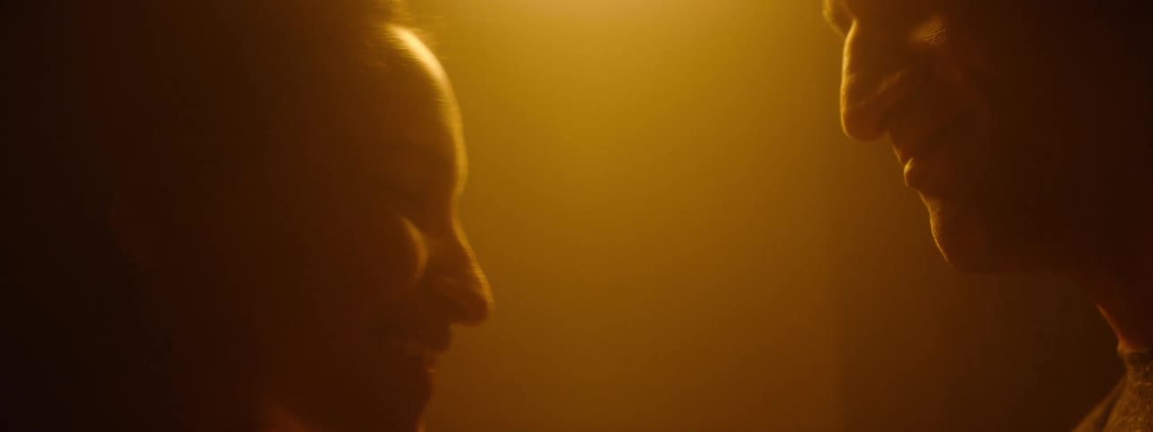 A woman smiles warmly as someone gently touches her face in soft golden light