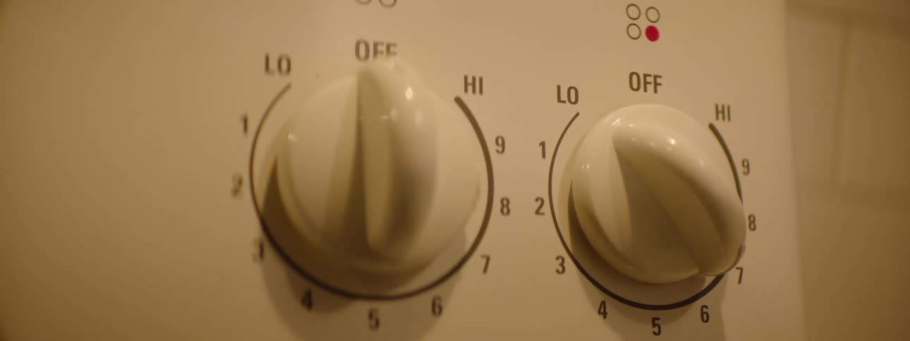 Hand turning a stove knob to adjust the temperature