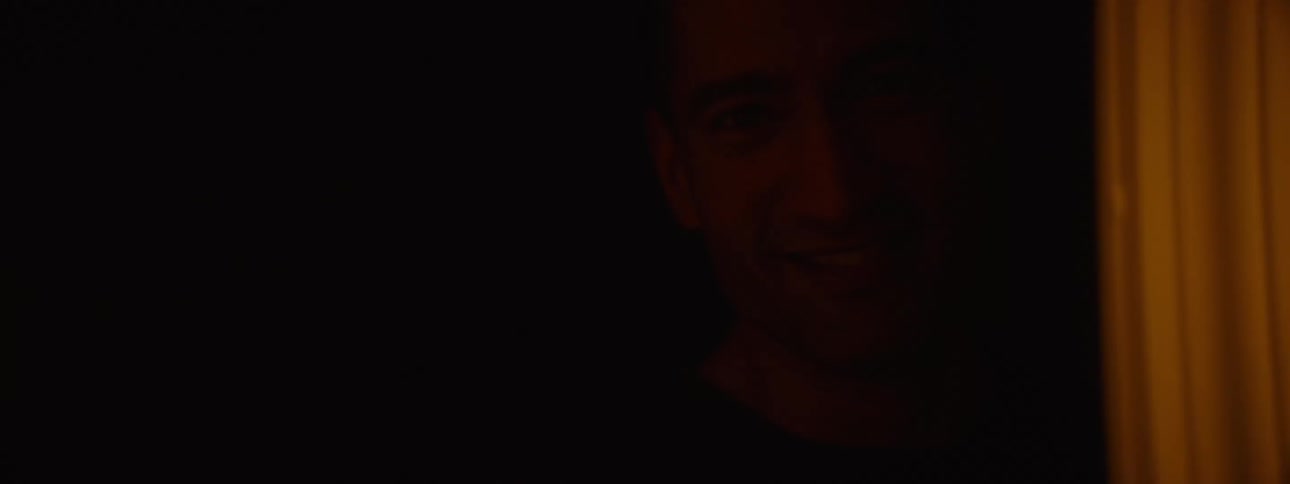 A persons face appears as a shadow in a doorway of darkness