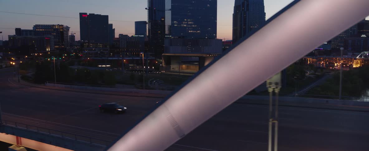 Car crosses the river via a bridge and travels past downtown in the evening