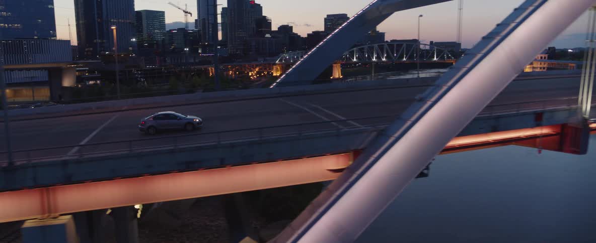 Aerial of a car moving across a bridge in a metropolitan city at sunset
