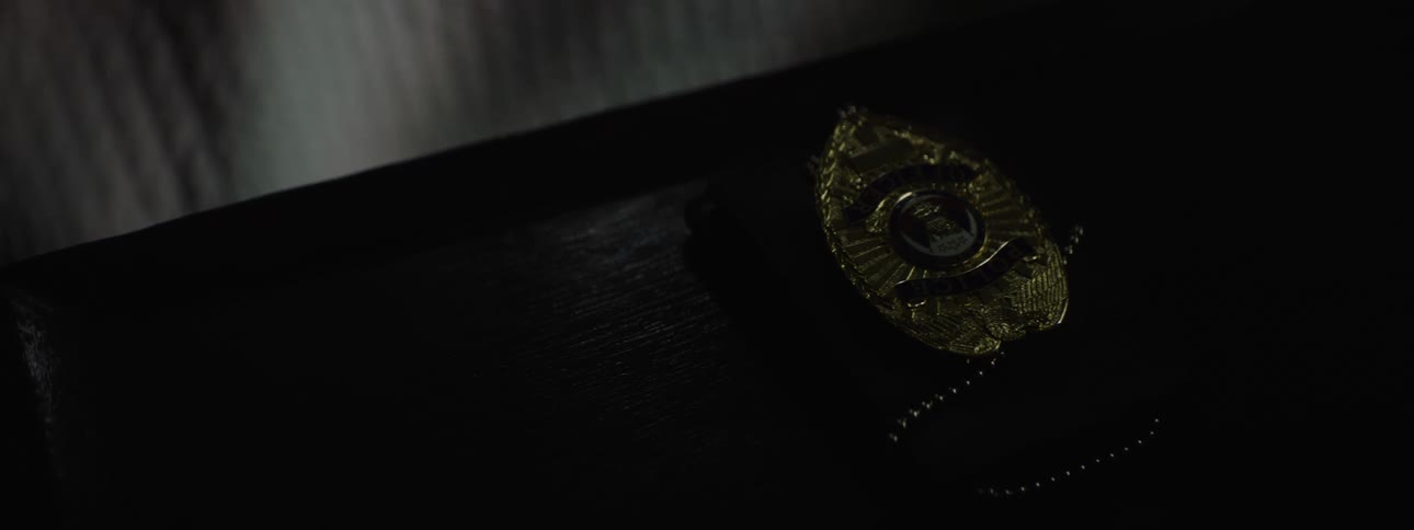 In the video a closeup shot shows a gold police badge with a chain lying on a dark textured surface the light catches the metal badge highlighting the intricate details of its design