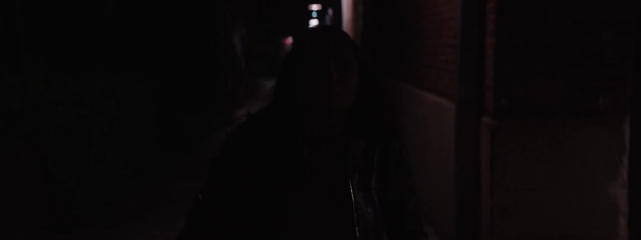 A young woman walks forward in a hallway in the dark